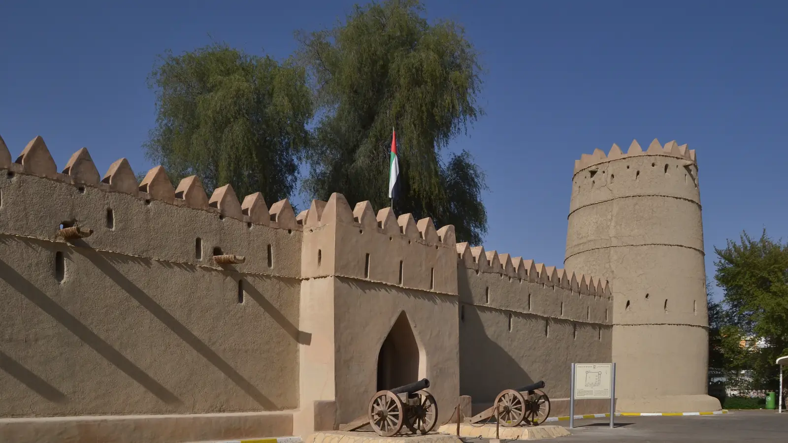 Forte Sheikh Sultan bin Zayed, em Al Ain, com muralhas de adobe ameadas, torre redonda, canhões antigos e a bandeira dos Emirados.