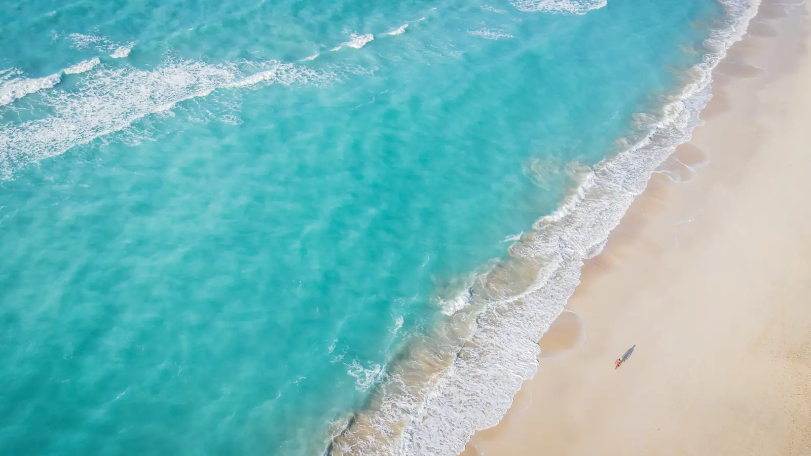 Vista aérea de uma praia da Ilha Saadiyat, com mar turquesa, ondas suaves e areia clara.