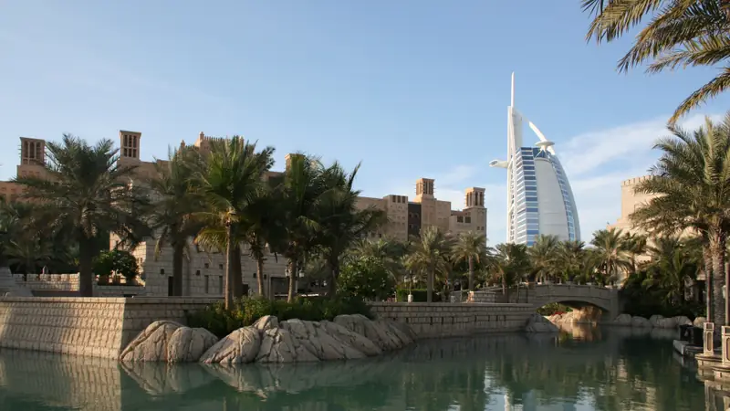 O Burj Al Arab em forma de vela visto de um canal do Madinat Jumeirah, entre palmeiras e torres de vento.