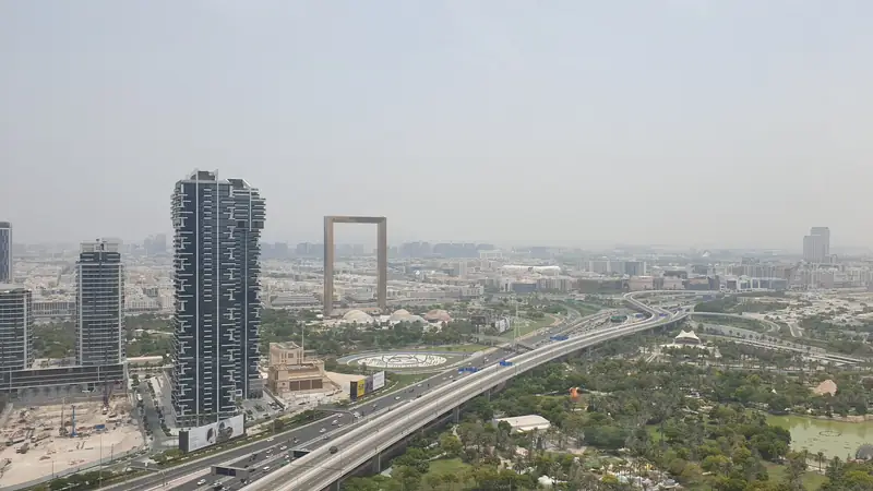Vista aérea em dia de bruma da Dubai Frame, a enorme moldura dourada no Zabeel Park, com uma avenida e torres em primeiro plano.