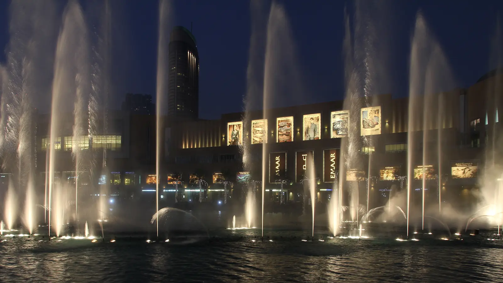 A Dubai Fountain à noite: jatos de água iluminados sobem diante da fachada acesa do The Dubai Mall.